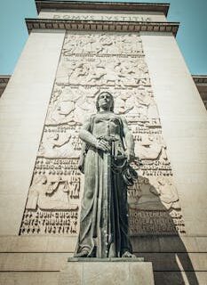 Statue of Justice on a courthouse facade, symbolizing law and order, under a clear blue sky.
