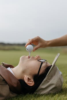 Unique concept photo of a person lying on grass with a golf tee and ball in mouth, showcasing sport and creativity.